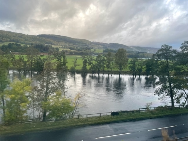 view from a train window looking down to a river, flooding its banks, with a road running alongside it