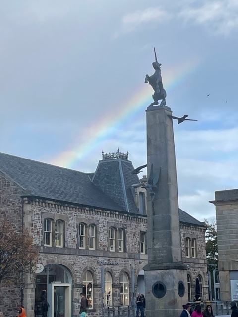 stone statue of a rearing unicorn, with a rainbow in the sky behind it